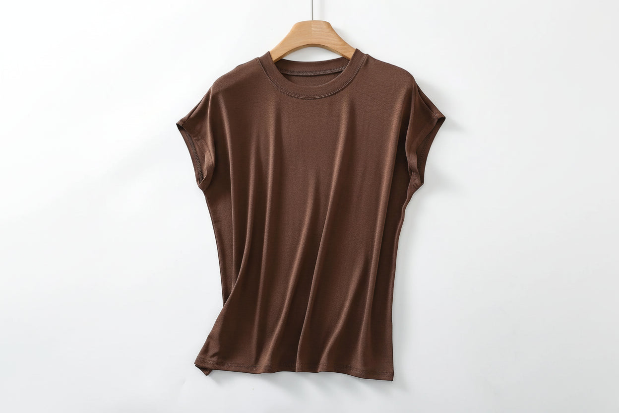 allvariants:: Brown t-shirt on a wooden hanger with magazines and a bowl of coffee beans on a white surface.