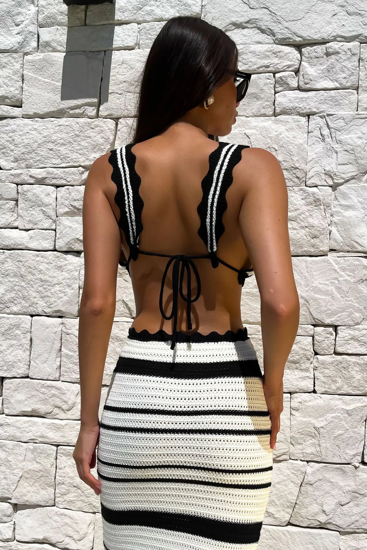 Black:: Woman wearing a black and white striped dress with open back against a stone wall.
