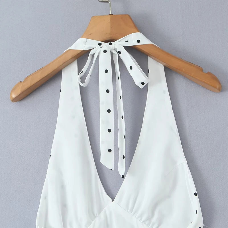 white::White halter top with black polka dots on a wooden hanger against a gray background