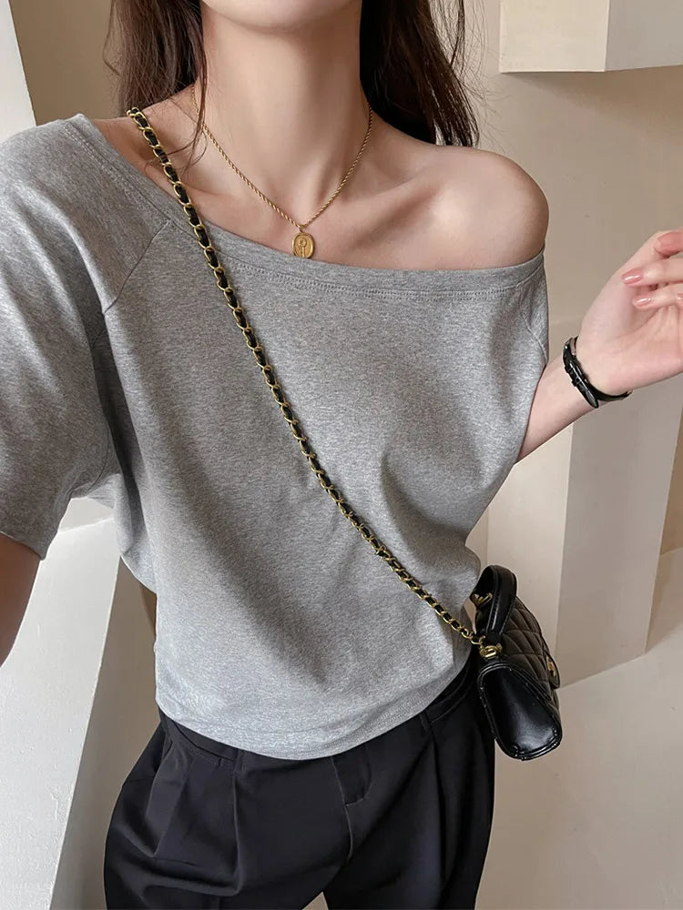 allvariants:: Person wearing a gray off-shoulder top and black pants, holding a black handbag with a gold chain strap.