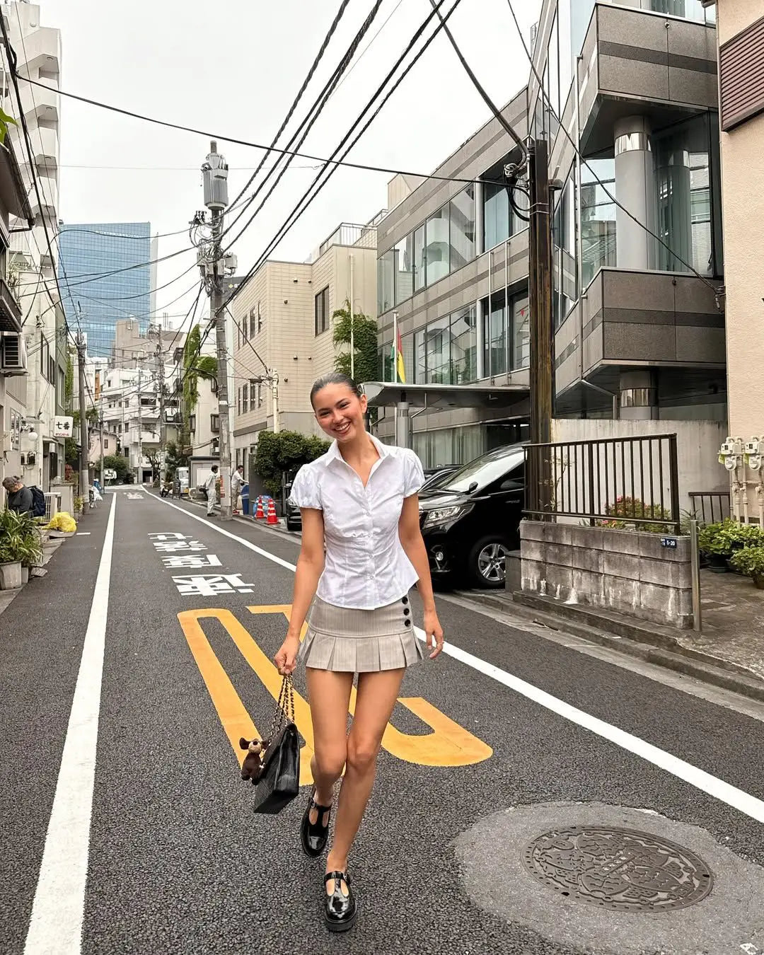 allvariant::Woman walking on a street in an urban area with modern buildings and power lines.