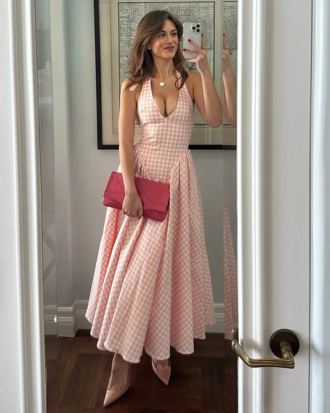 pink::Woman in a pink checkered dress holding a pink clutch in front of a mirror.
