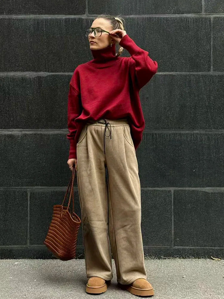 allvariants:: Person wearing a red sweater and beige pants against a black brick wall.