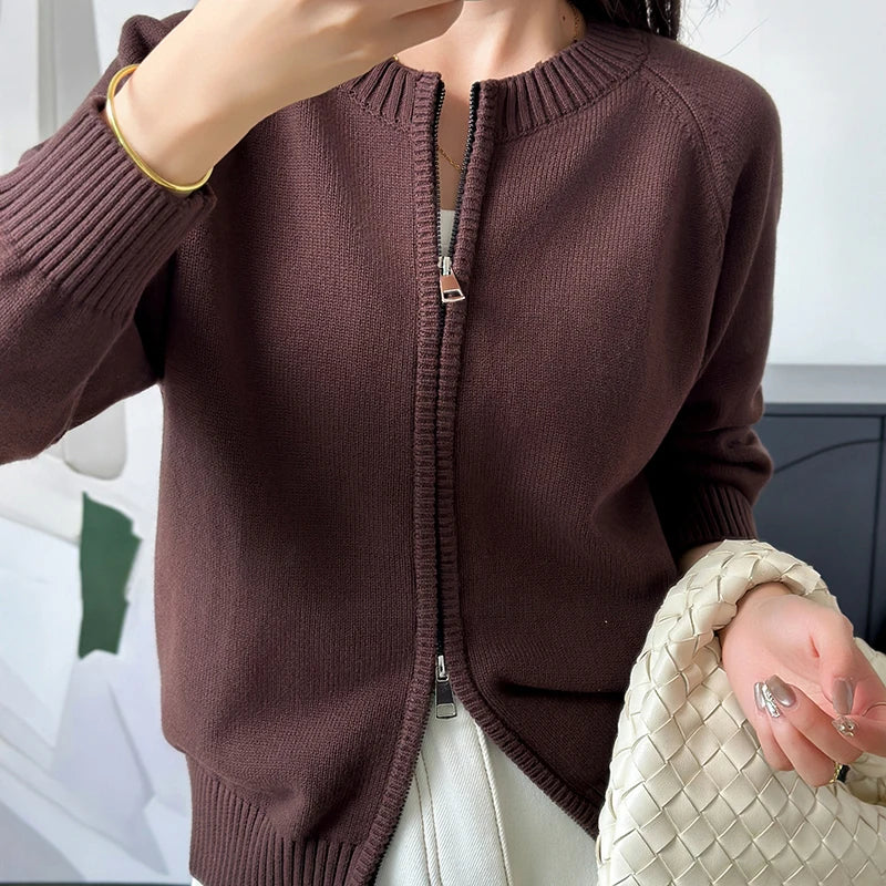 allvariants:: Person wearing a brown zip-up sweater holding a beige handbag indoors.