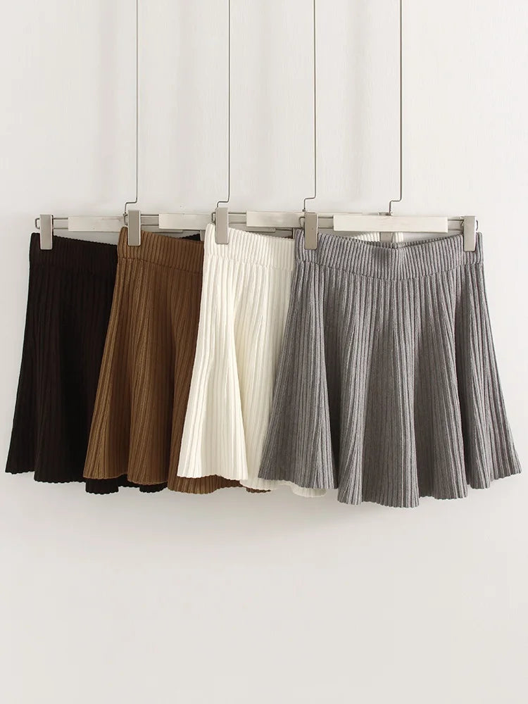 allvariants:: Four pleated skirts in black, brown, white, and gray hanging on a rack against a white background.
