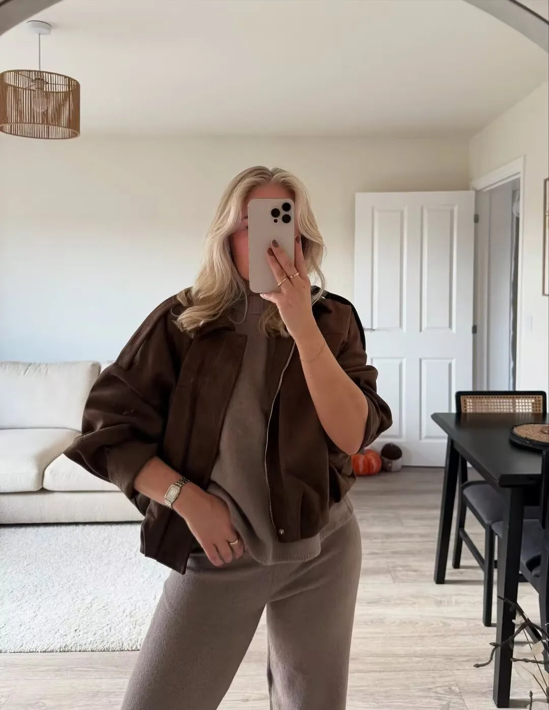 allvariant::Person taking a mirror selfie in a living room wearing a brown jacket and gray pants.