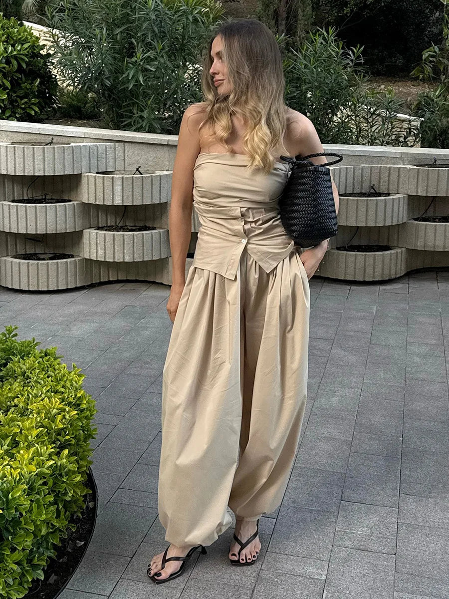 khaki::Woman in a beige strapless dress holding a black bag outdoors.