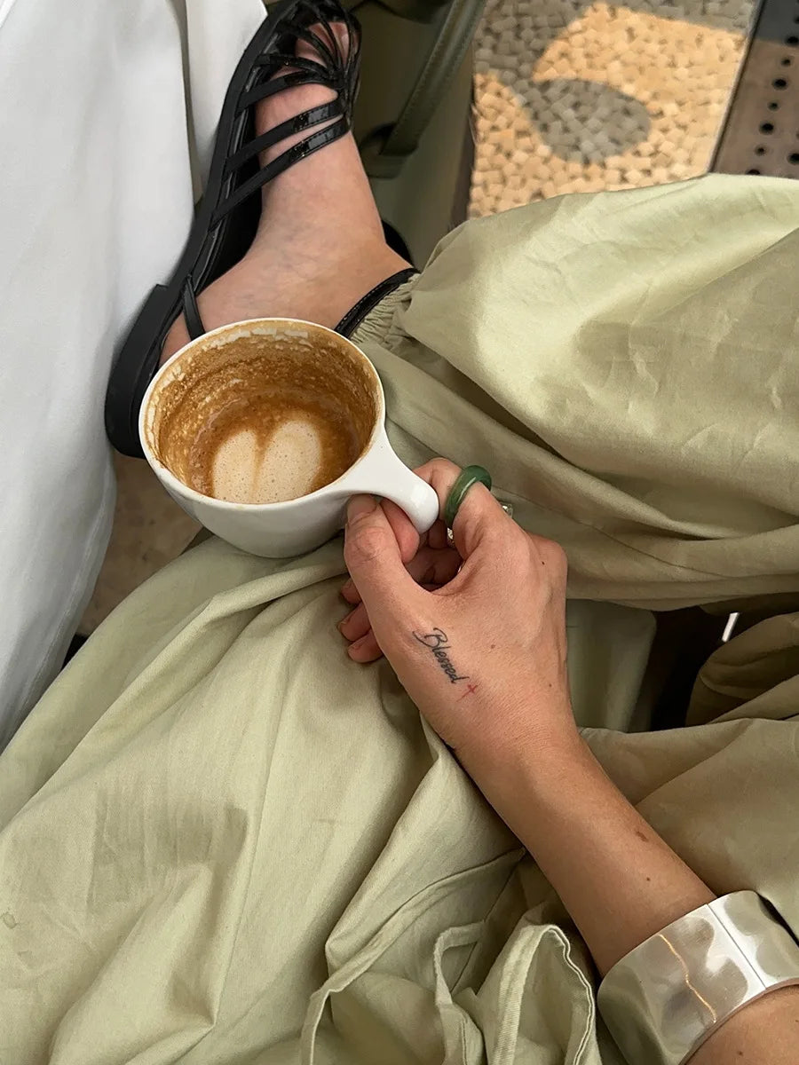 Green::Person holding a cup of coffee with a latte art heart, sitting on a textured surface.
